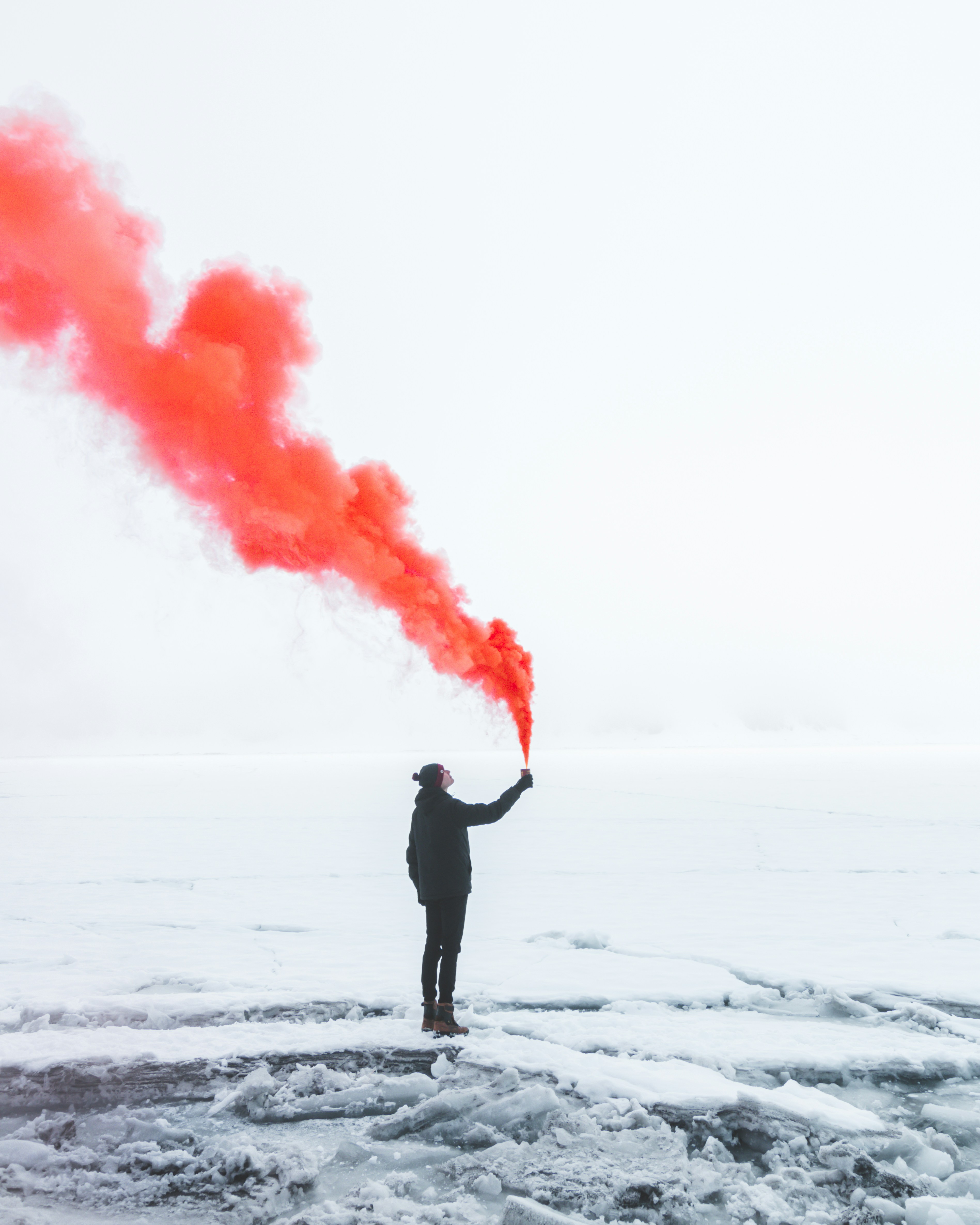 Person standing on a frozen landscape holding a red smoke flare